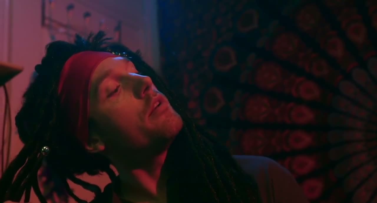 Christopher Adams in character, dreadlocks and a red headband, under red light
