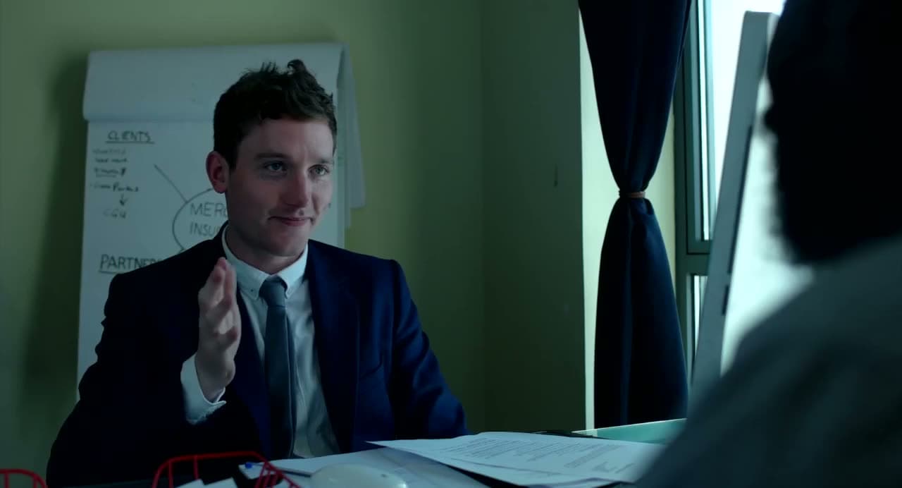 Christopher Adams in a suit at a desk, making a point